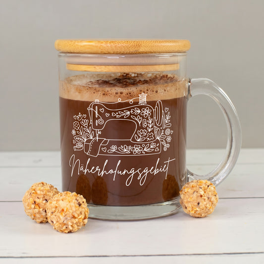 Glastasse mit Kakao, Bambusdeckel und weißem „Näherholungsgebiet“ Nähmotiv neben kleinen Pralinen