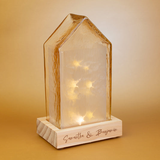LED-Haus von Leonardo mit warmem Amberlicht und personalisierter Gravur auf dem Holzsockel – dekorative Glaslampe im modernen Hausdesign auf goldfarbenem Hintergrund.