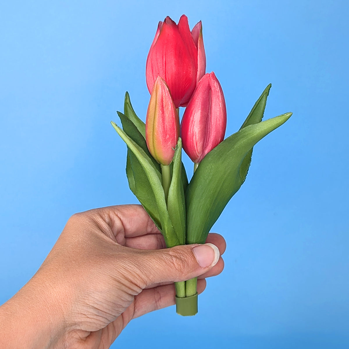 Kunstblumenstrauß aus drei rosa Tulpen in Hand gehalten