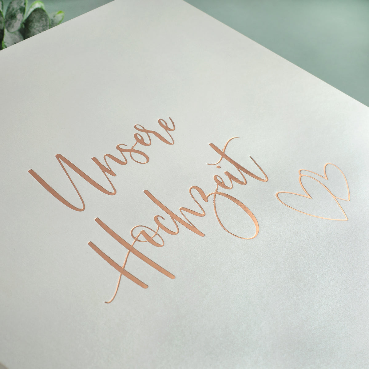 Nahaufnahme des Hochzeitsalbums mit geprägtem Schriftzug „Unsere Hochzeit“ in edler Goldprägung und zwei Herzen.
