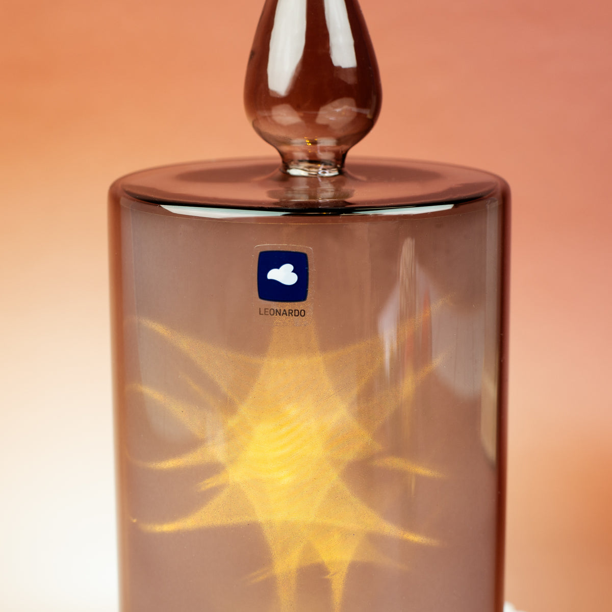 Seitliche Detailansicht der Leonardo LED-Kerze mit sichtbarem Herstellerlogo und warm leuchtendem LED-Licht im grauen Glas.