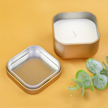 Goldene Mini Duftkerze mit geöffnetem Deckel und weißem Wachs auf gelbem Hintergrund mit Eukalyptus-Deko