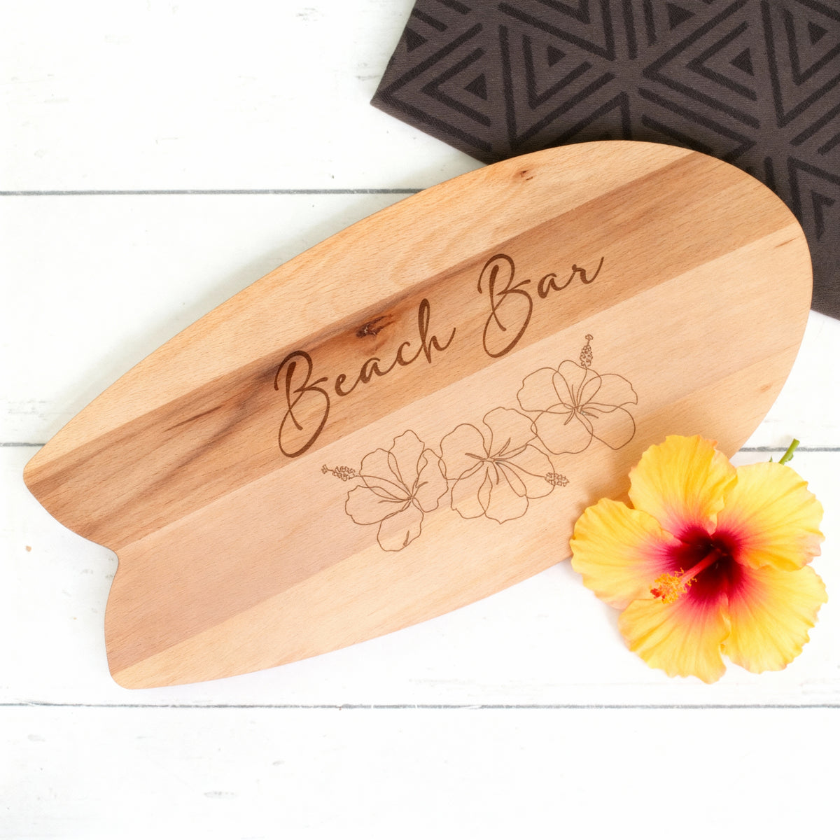 Surfbrett-Servierbrett aus Holz mit Hibiskusgravur und gelber Blüte als sommerliche Dekoration