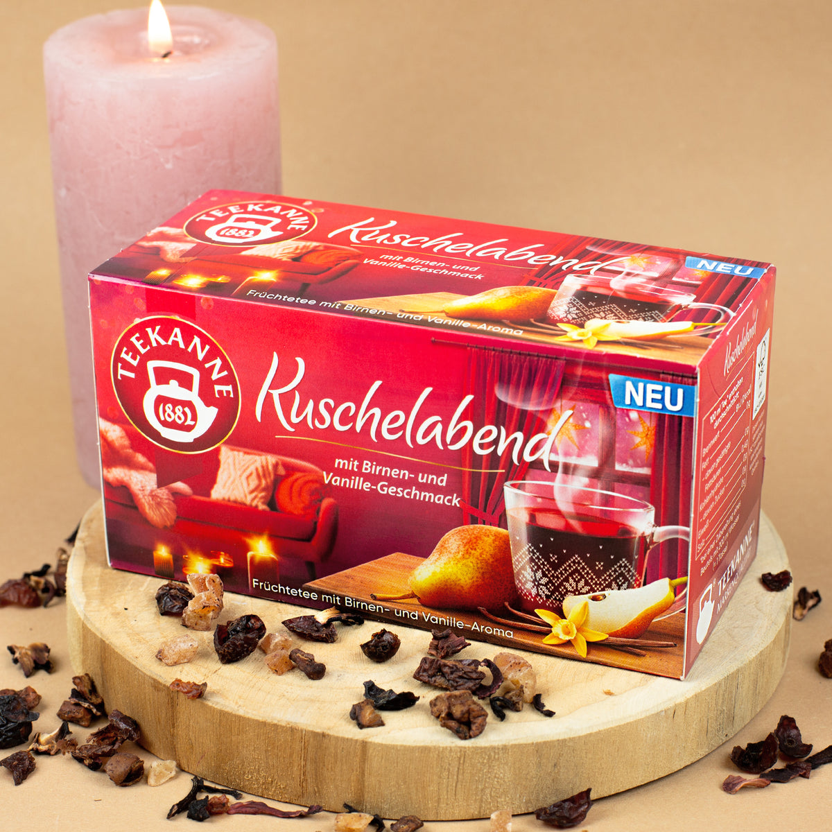Packung „Teekanne Kuschelabend“ auf Holzscheibe platziert, dekoriert mit losen Teestückchen.