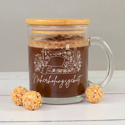 Glastasse mit Kakao, Bambusdeckel und weißem „Näherholungsgebiet“ Nähmotiv neben kleinen Pralinen