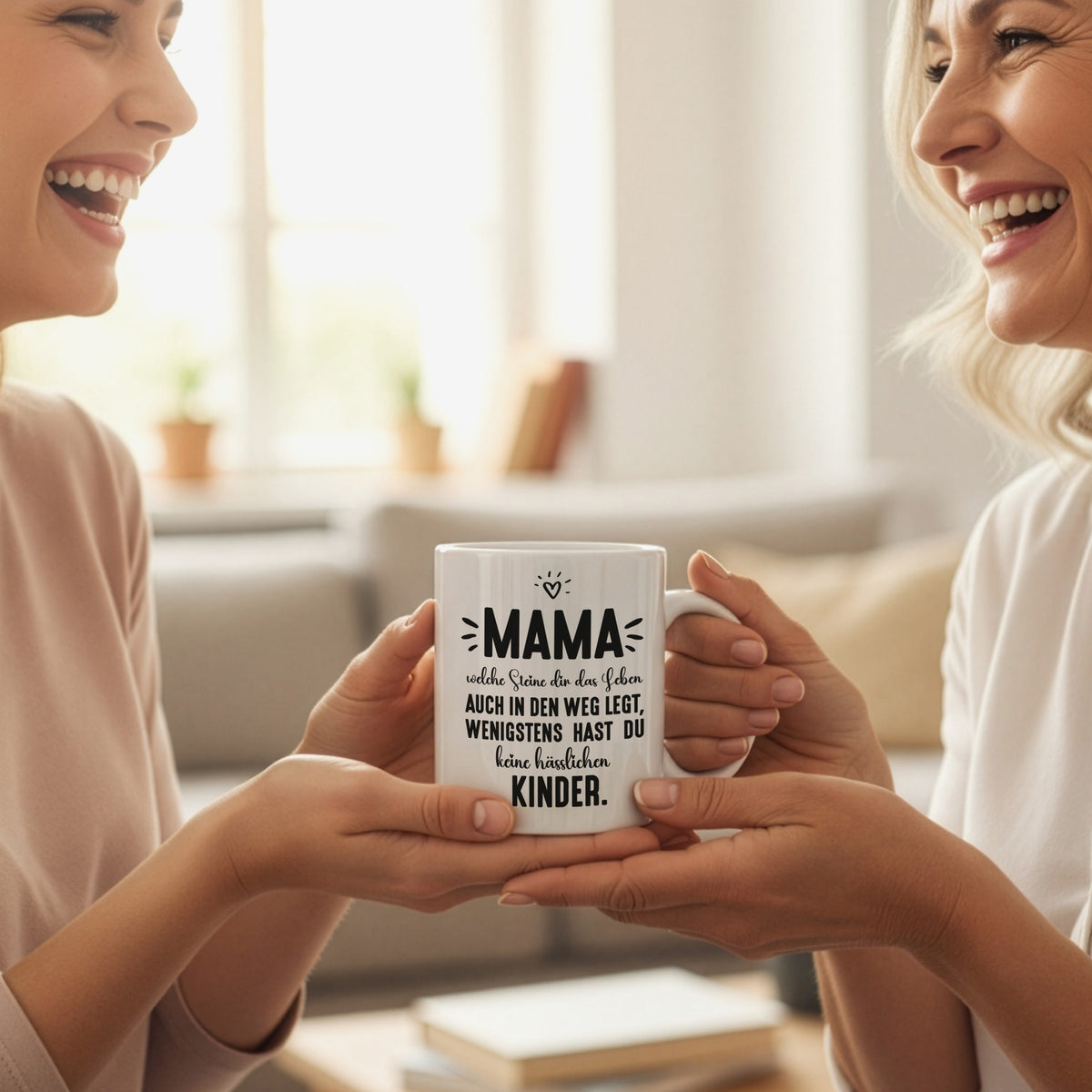 Zwei Frauen überreichen sich lachend eine weiße Keramiktasse mit Mama-Spruch als Geschenk in wohnlicher Umgebung