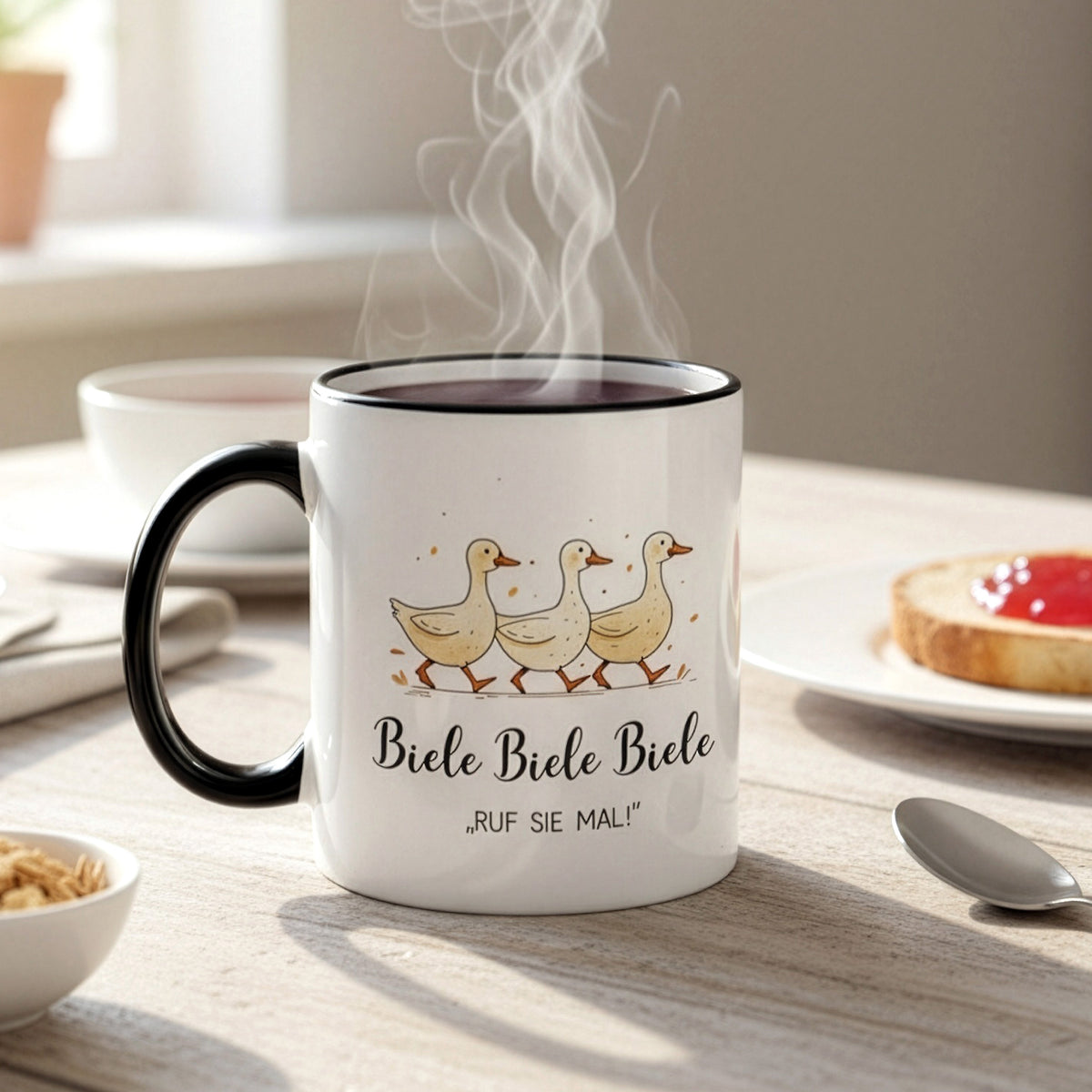 Dampfende Tasse mit Entenmotiv „Biele Biele Biele – Ruf sie mal!“ auf Frühstückstisch mit Marmeladentoast und Besteck – warme Lichtstimmung.