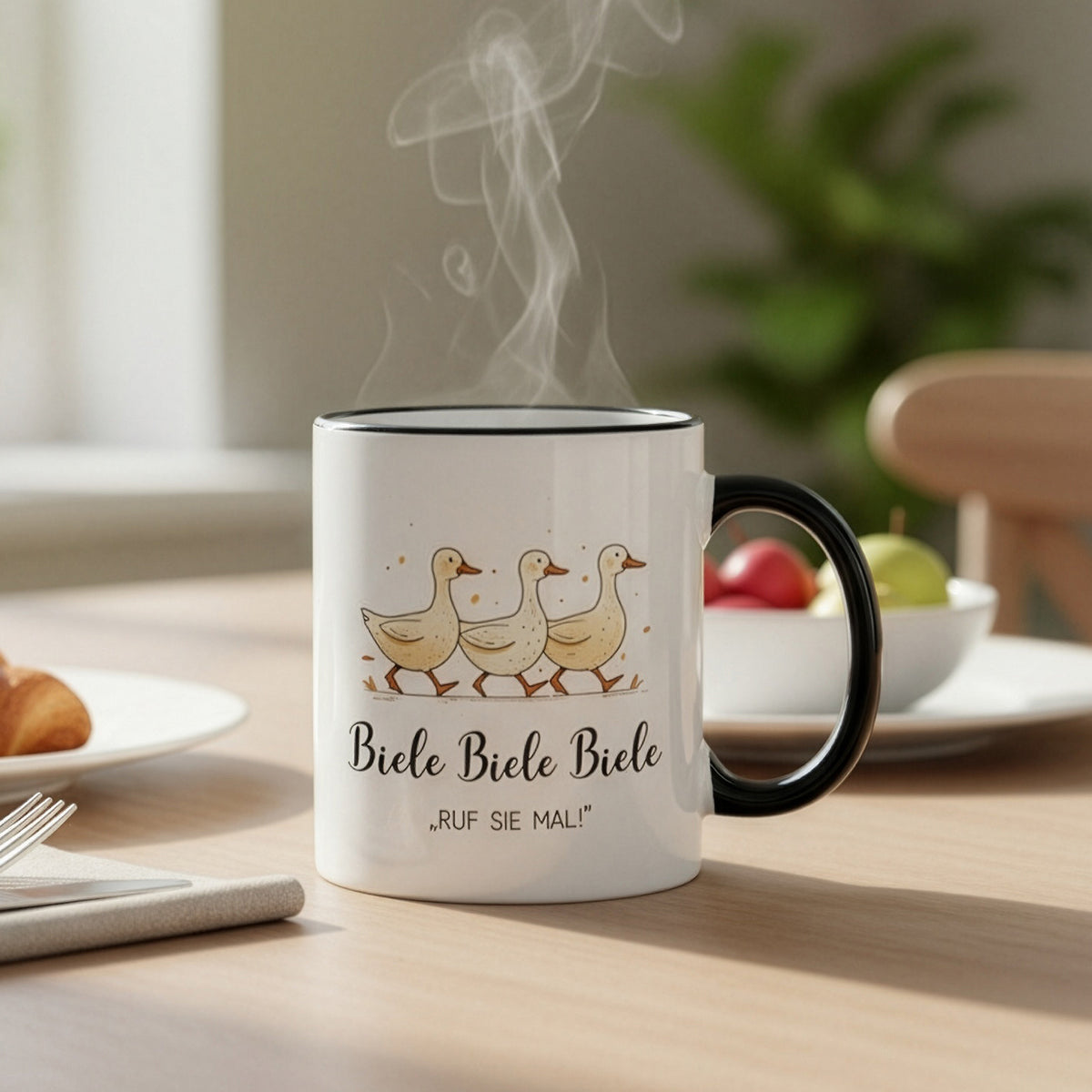Dampfende Tasse mit Entenmotiv „Biele Biele Biele – Ruf sie mal!“ auf Frühstückstisch mit Obstschale – gemütliche Atmosphäre.