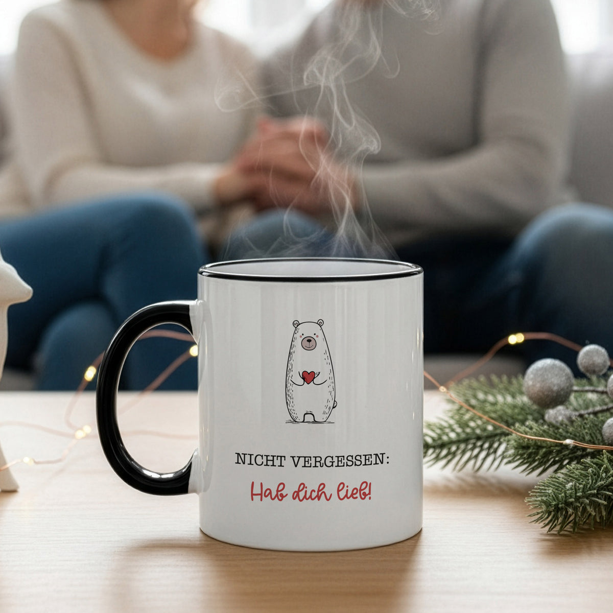 Dampende Keramiktasse mit „Hab dich lieb“-Spruch auf einem Tisch, im Hintergrund ein Paar und Winterdeko.