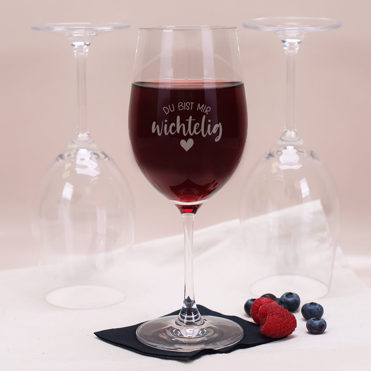 Weinglas aus robustem Teqton-Glas mit Gravur „Du bist mir wichtelig“, gefüllt mit Rotwein, vor umgedrehten Leonardo-Gläsern.