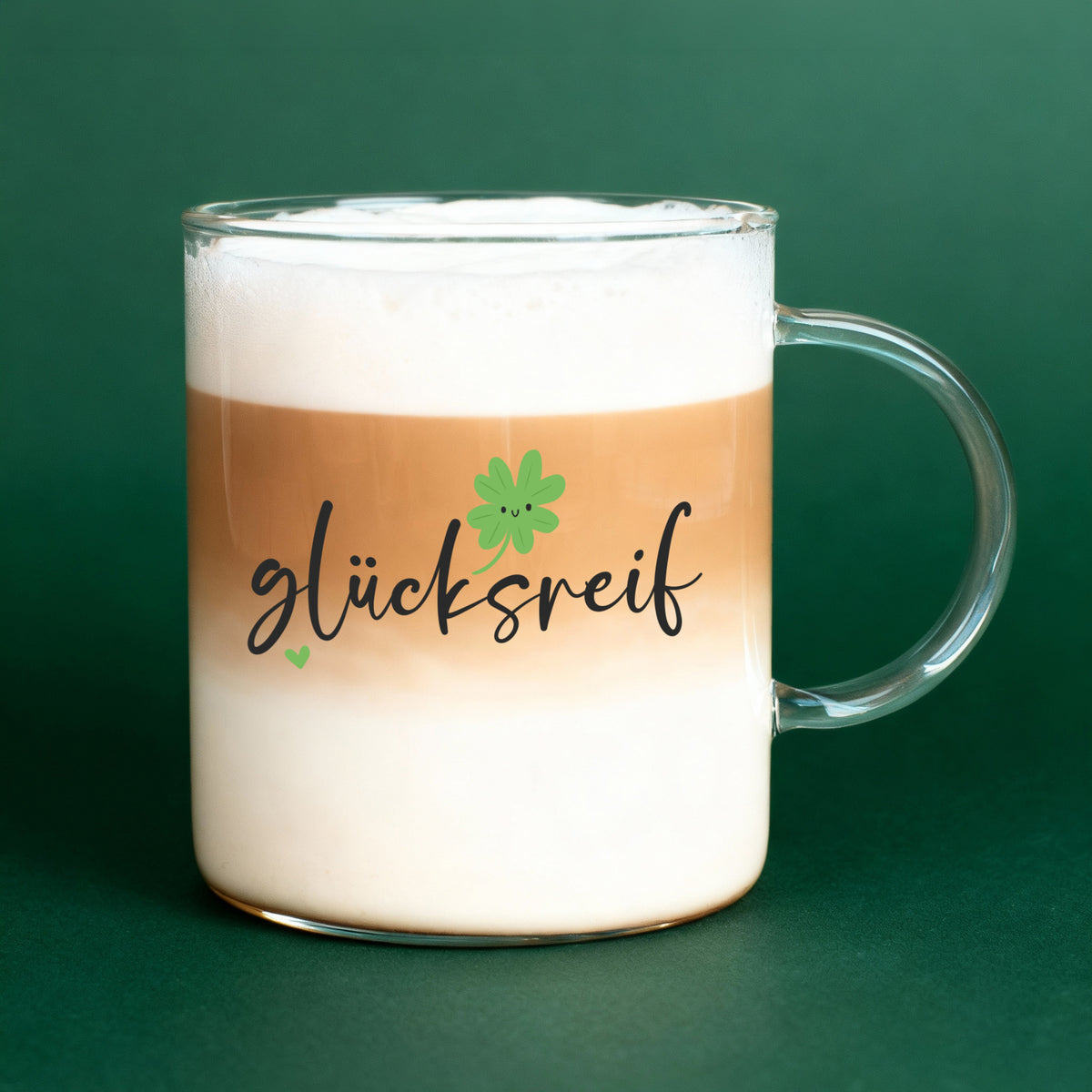 Leonardo-Teeglas „glücksreif“ gefüllt mit Latte Macchiato vor grüner Hintergrundkulisse