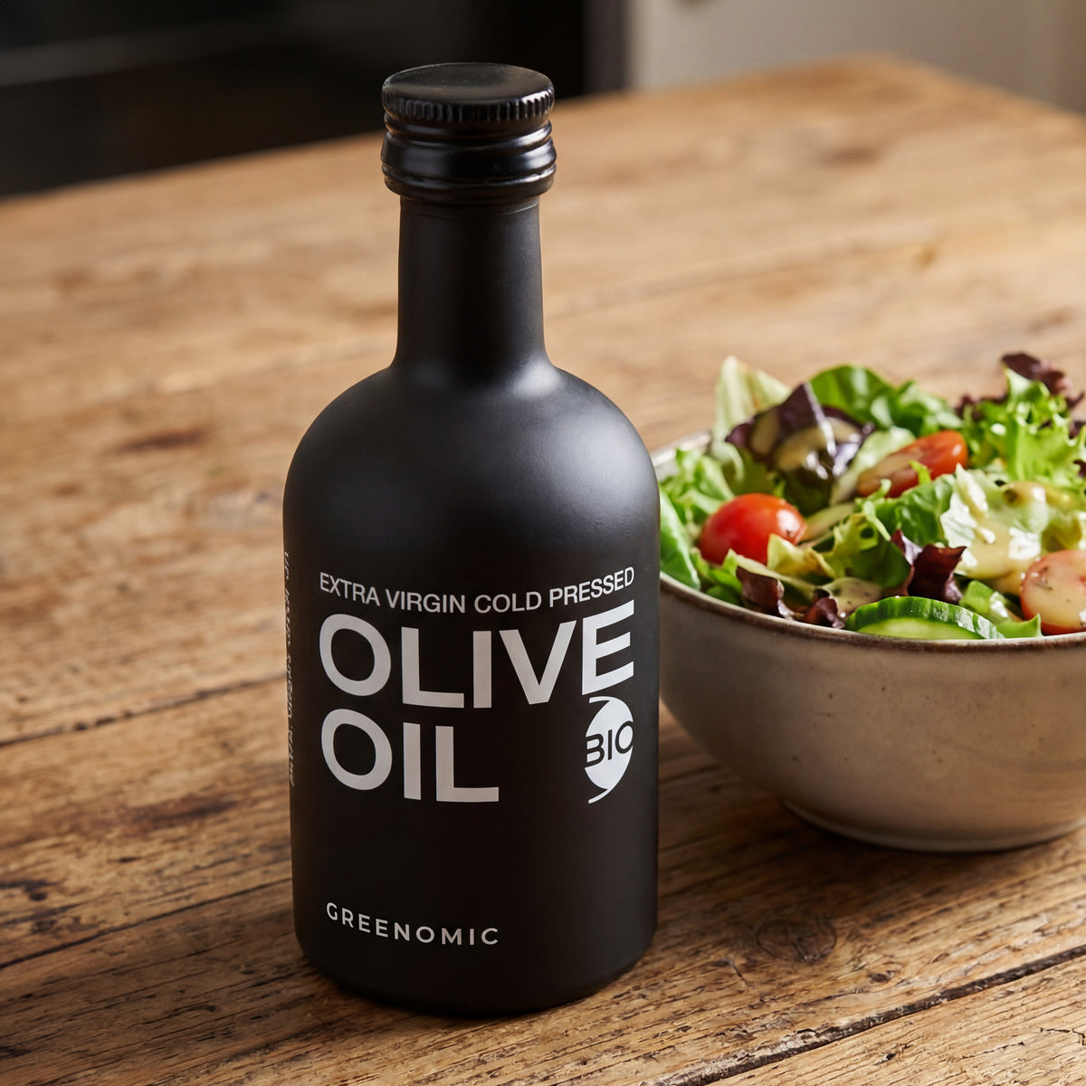 Schwarzes Olivenöl nativ extra in edler Flasche neben Salatschüssel auf Holztisch