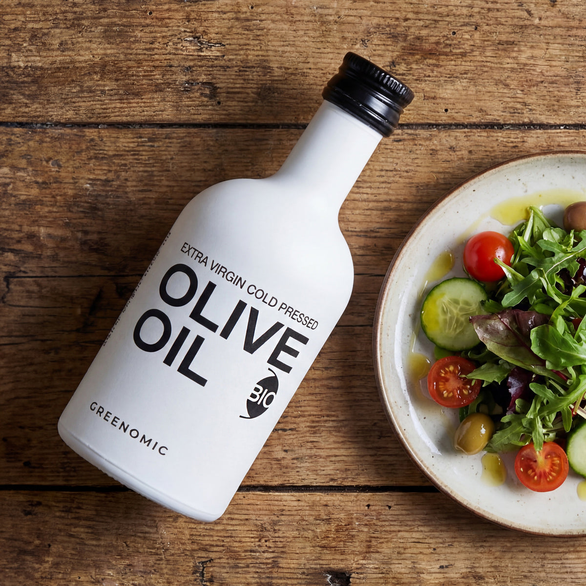 Weißes BIO Olivenöl in moderner Flasche als Geschenk neben Salat auf Tisch