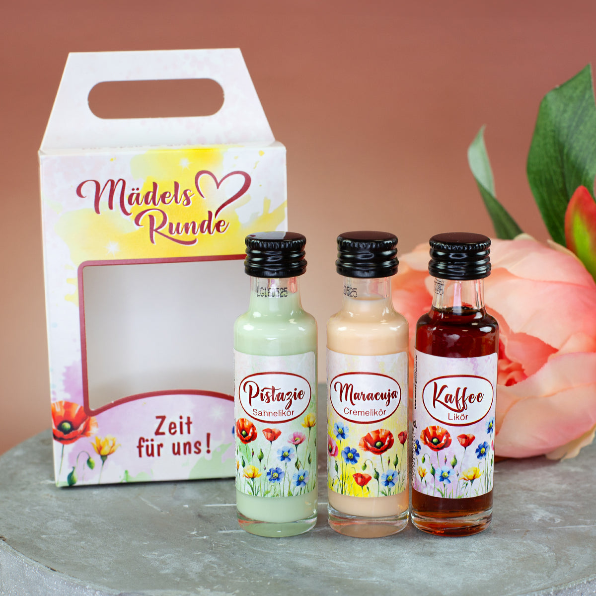 Likör Geschenkset „Mädelsrunde“ mit drei Mini-Flaschen vor Geschenkverpackung und Blumenmotiv