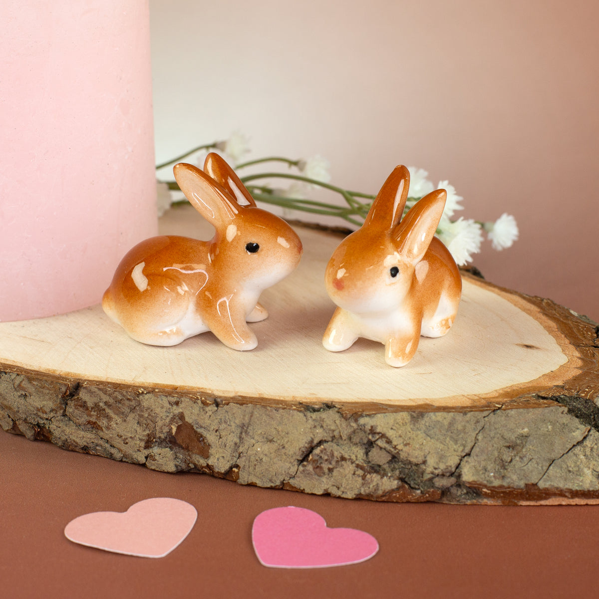 Kleines Keramik-Häschen braun-weiß als Osterdeko neben Kerze auf Holzscheibe