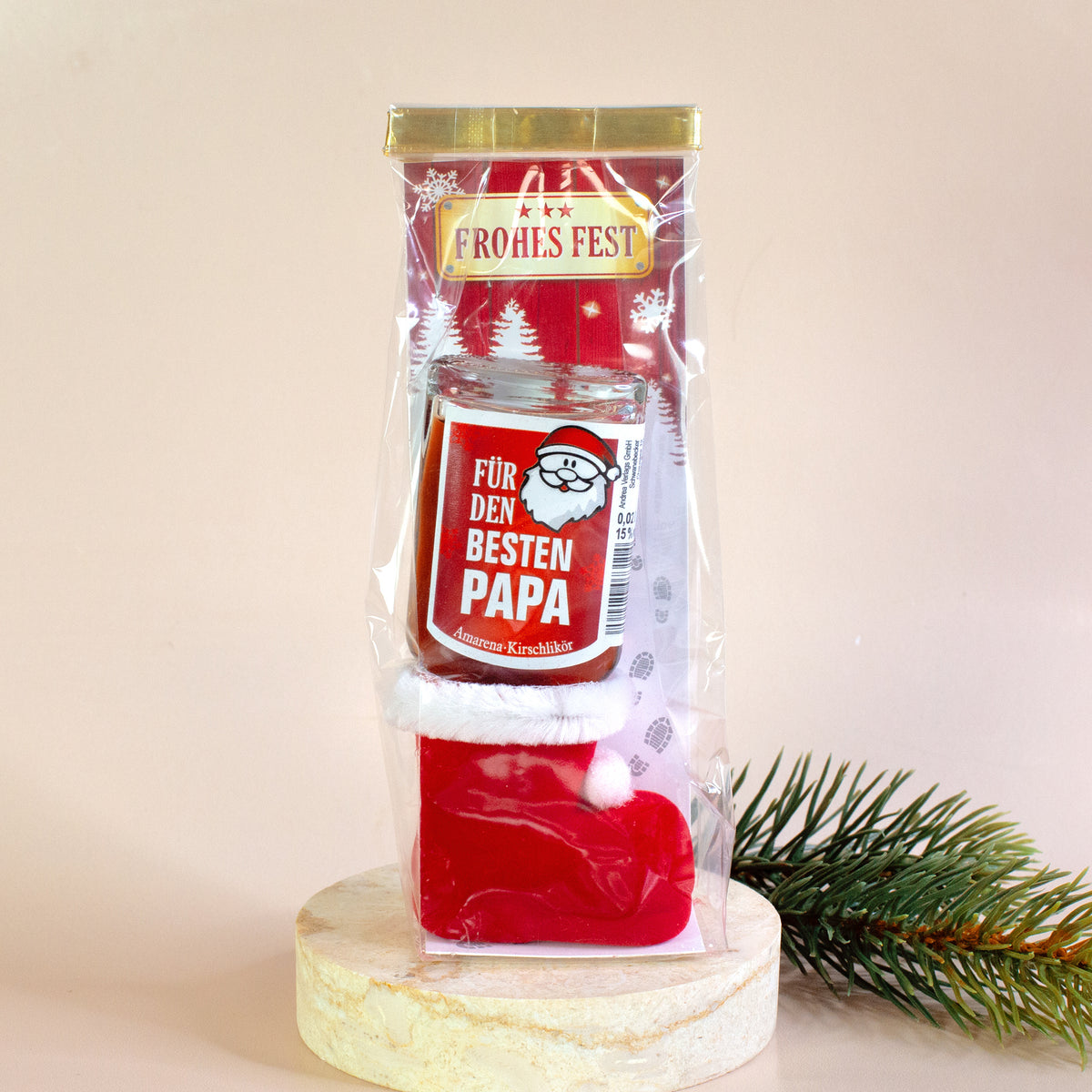 Einzelansicht des verpackten Stiefels mit der Flasche „Für den besten Papa“. Der Stiefel steht auf einem runden Marmorsockel, im Hintergrund Tannenzweig und zart rosafarbener Hintergrund.