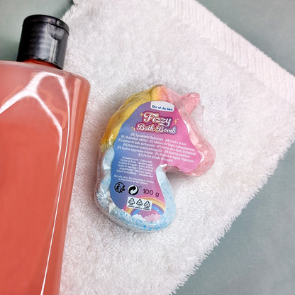 Einhorn-Badekugel mit Etikett auf weißem Handtuch neben einer großen Duschgel-Flasche