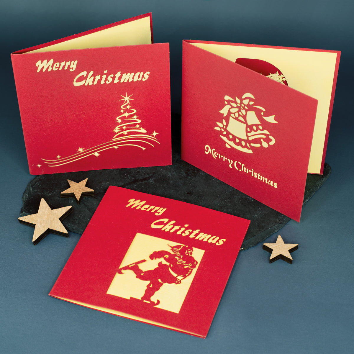 Drei rote Weihnachtskarten mit goldgelbem Innenleben und „Merry Christmas“-Schriftzug in verschiedenen Designs – Weihnachtsmann, Glocken und Tannenbaum.