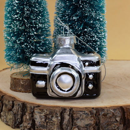 Schwarz-silberne Kamera als Retro Glas Weihnachtsbaumschmuck zwischen verschneiten Tannen