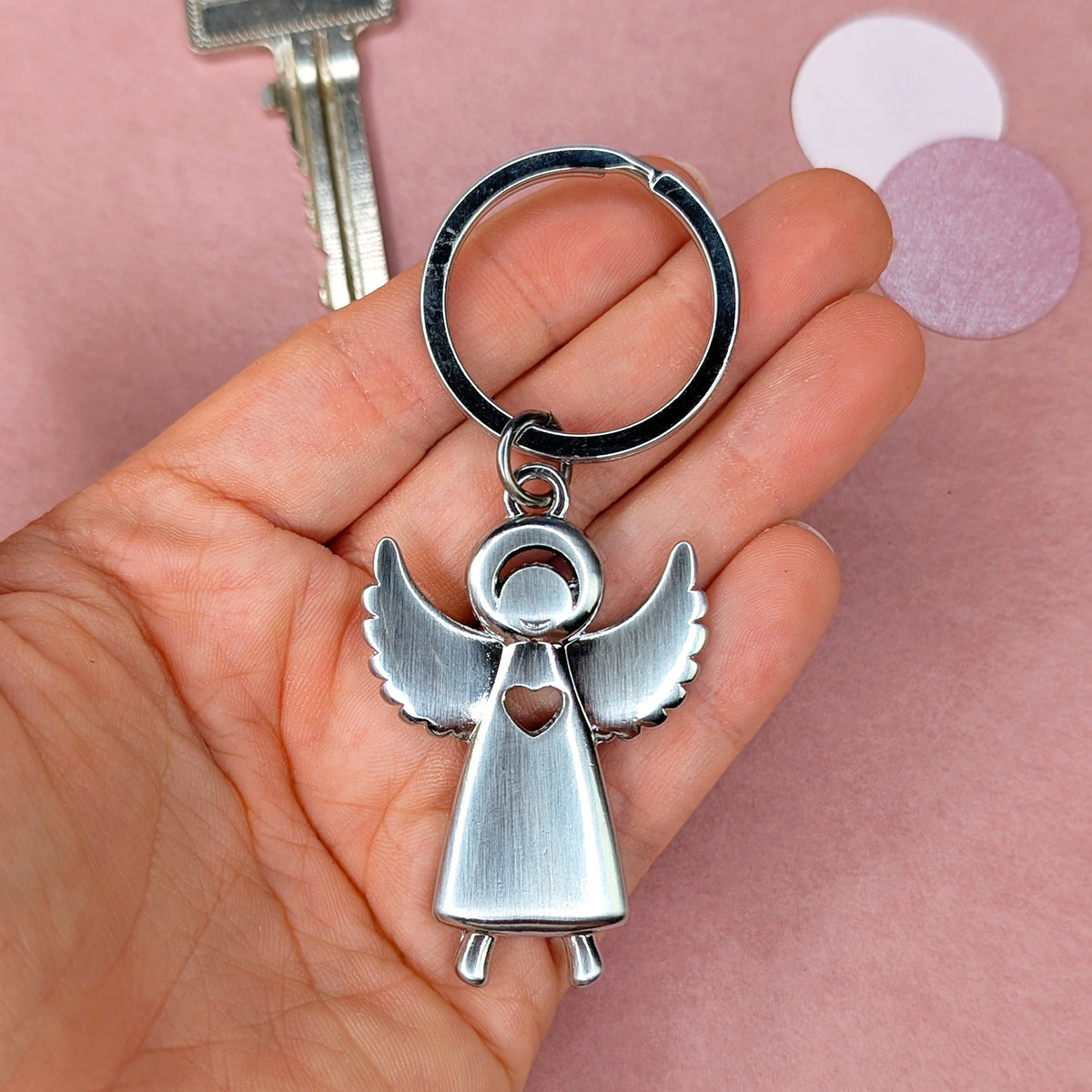 Schlüsselanhänger in Engel-Form aus silberfarbenem Metall, gehalten in einer Hand, mit Herz-Aussparung im Körper und Flügeln nach oben