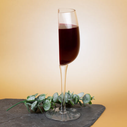 Halbes Weinglas aus transparentem Glas mit rotem Wein, dekorativ auf Schieferplatte arrangiert, humorvoller Scherzartikel