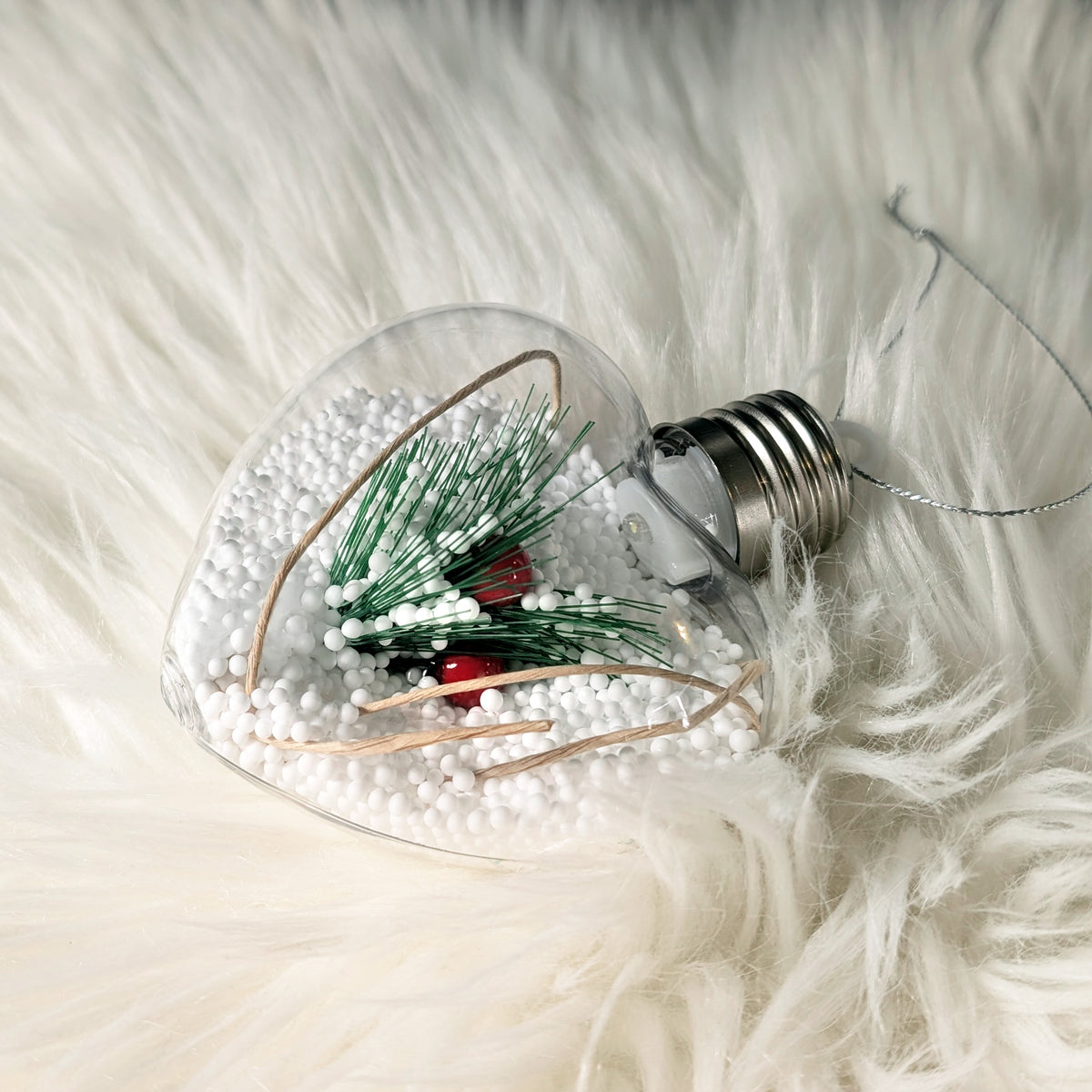 Herzförmige Weihnachtskugel mit LED-Beleuchtung, Schneeoptik und feiner Aufhängung auf weißem Fell.