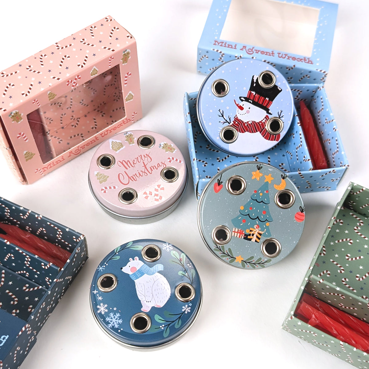 Vier verschiedene Mini-Adventskränze mit Motiven „Schneemann“, „Weihnachtsbaum“, „Eisbär“ und „Merry Christmas“, jeweils mit passenden Geschenkverpackungen und roten Mini-Kerzen, auf weißem Hintergrund.