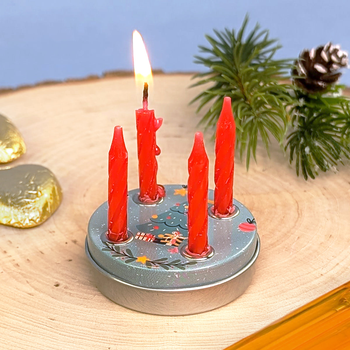 Mini-Adventskranz im Weihnachtsbaum-Design mit vier roten Kerzen, eine davon brennend, arrangiert auf hellem Holz mit Weihnachtsdeko.