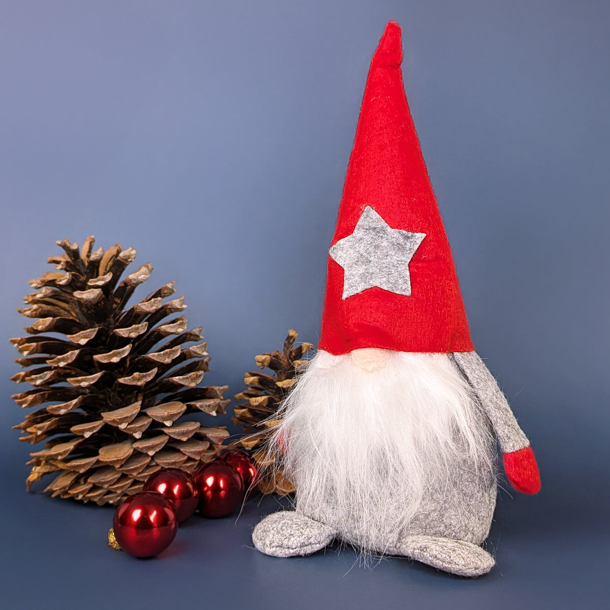 Weihnachtswichtel mit roter Filzmütze und langem Bart vor Tannenzapfen und Weihnachtskugeln