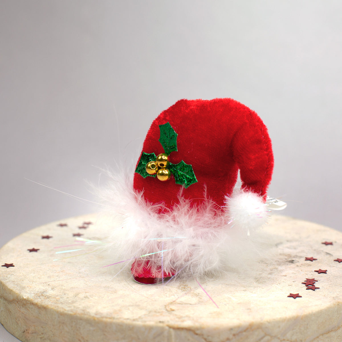 Nahaufnahme eines roten Plüsch-Haarclips in Form einer Weihnachtsmütze mit weißem Flaum und Glöckchen-Deko.