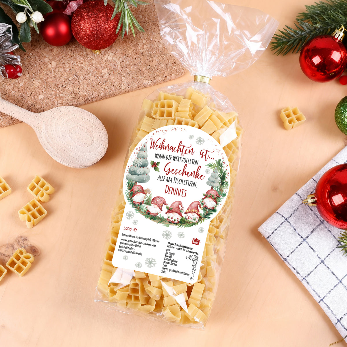 Weihnachtsnudeln mit Etikett „Dennis“, dekoriert mit Kugeln und Holzlöffel auf Holztisch
