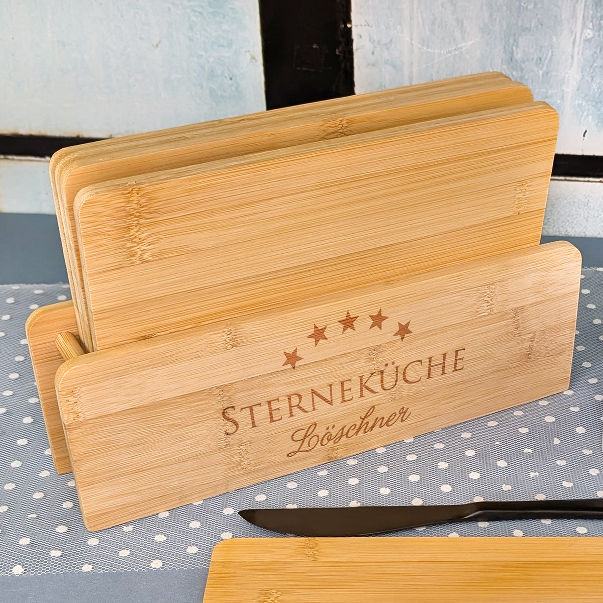 Bambusbrettchen-Set im Halter mit Gravur „STERNEKÜCHE“ und Name „Löschner“ auf gepunktetem Tuch