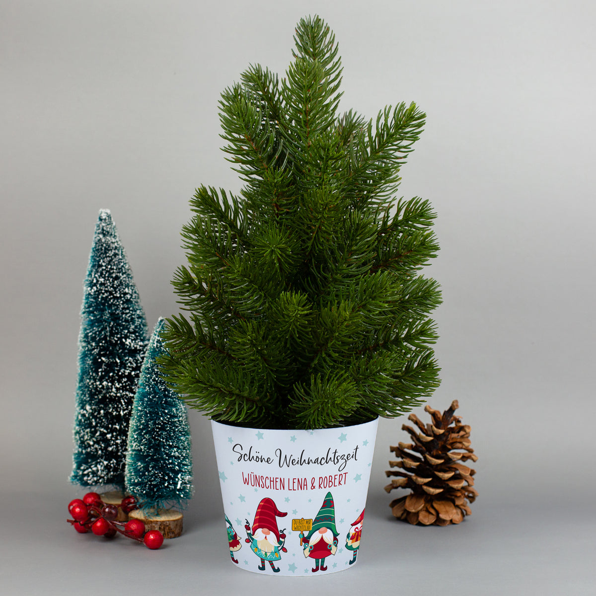 Mini-Weihnachtsbaum im Topf mit personalisierter Wichtel-Banderole und festlicher Deko im Hintergrund