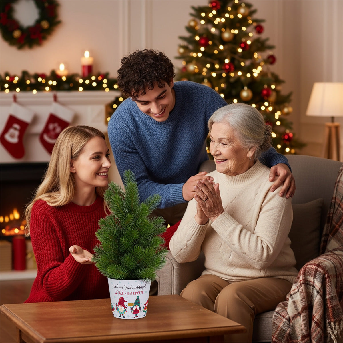 Familienmoment zu Weihnachten: Enkel und Oma freuen sich gemeinsam über einen personalisierten Mini-Weihnachtsbaum mit Wichtel-Banderole auf dem Tisch, festlich dekorierter Raum im Hintergrund.