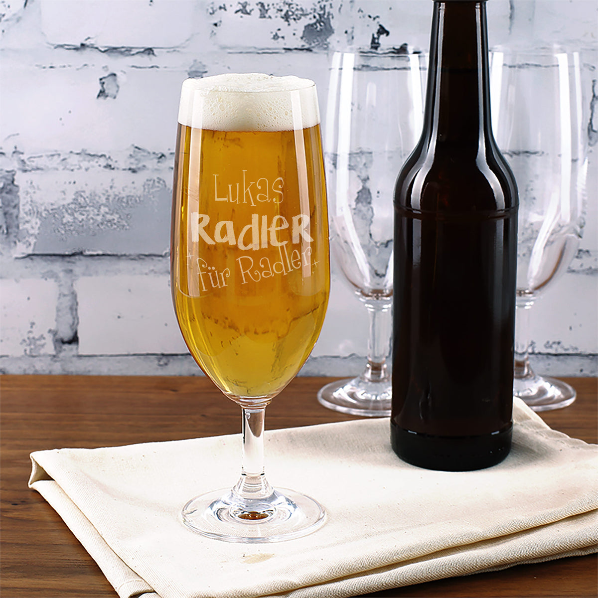 Personalisiertes Bierglas „Radler für Radler“ mit Gravur vor Flasche Bier auf weißem Tuch