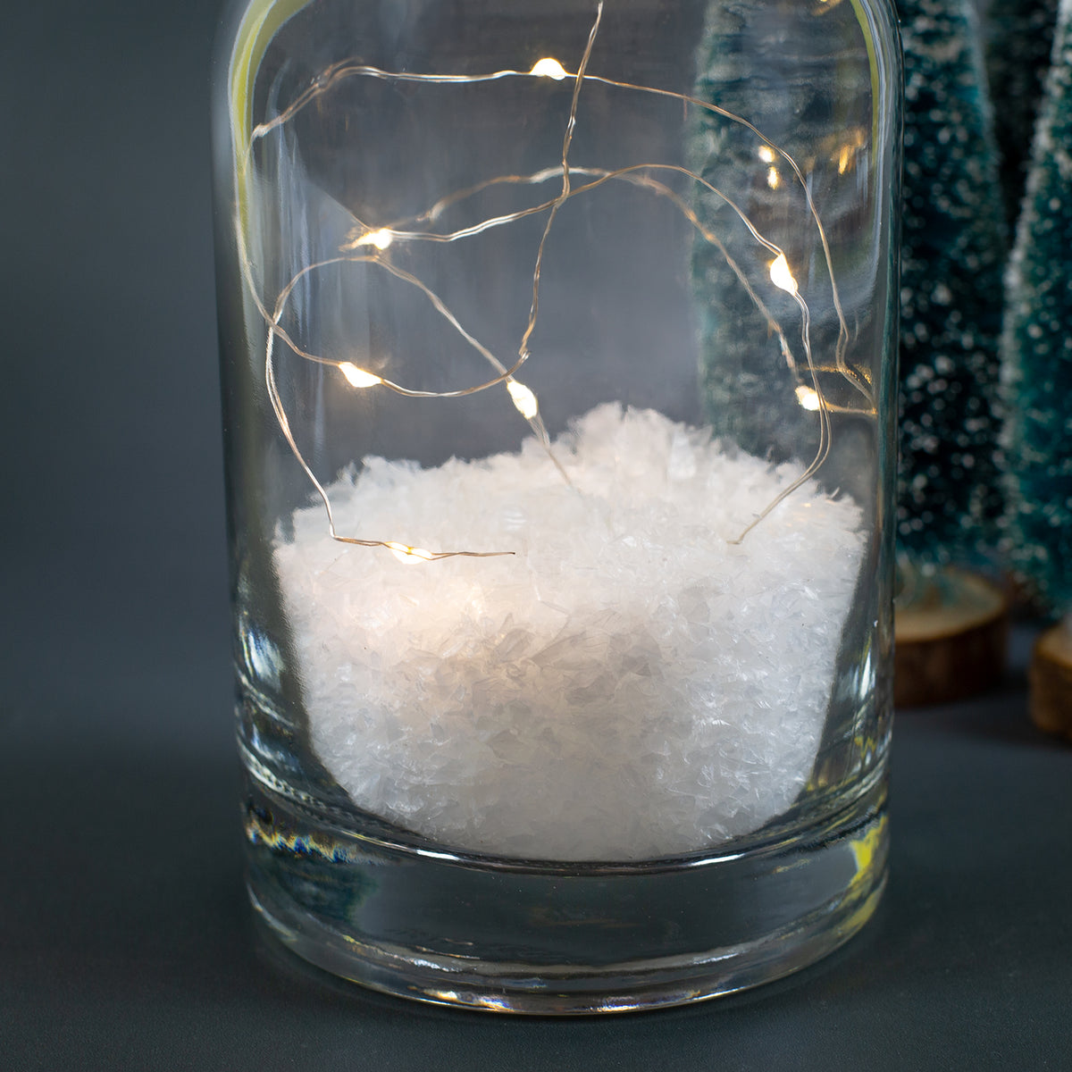 Detailaufnahme der Deko-Karaffe mit Kunstschnee und LED-Lichterkette im Inneren, warmweiße Lichtpunkte vor dunklem Hintergrund.