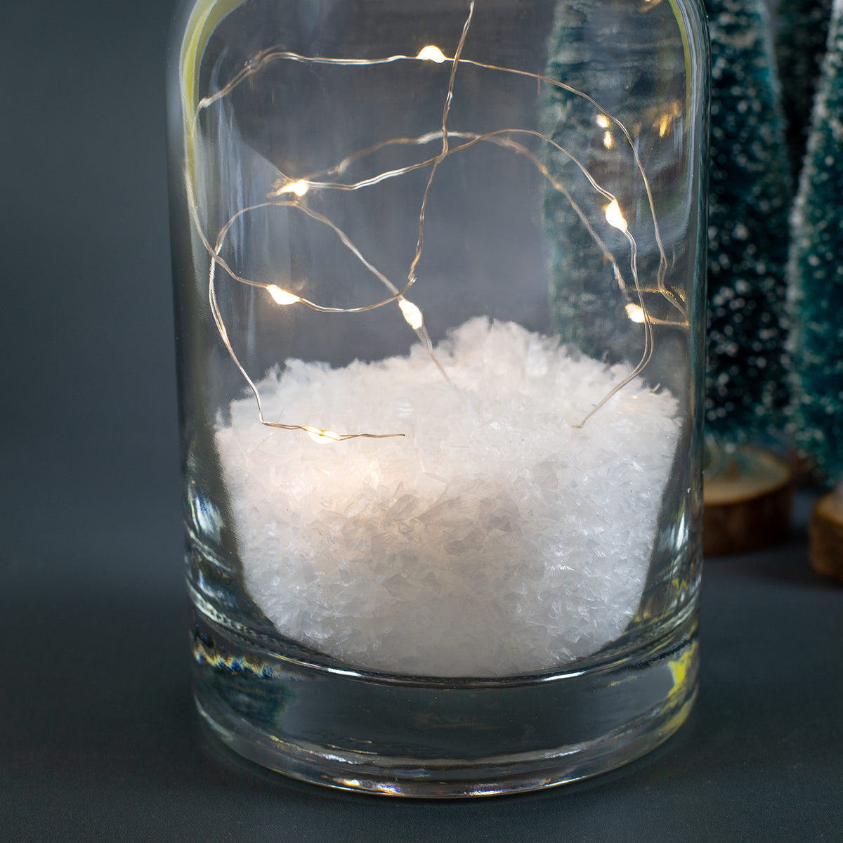 Detailaufnahme von Kunstschnee und LED-Lichterkette im Inneren der Glasflasche.