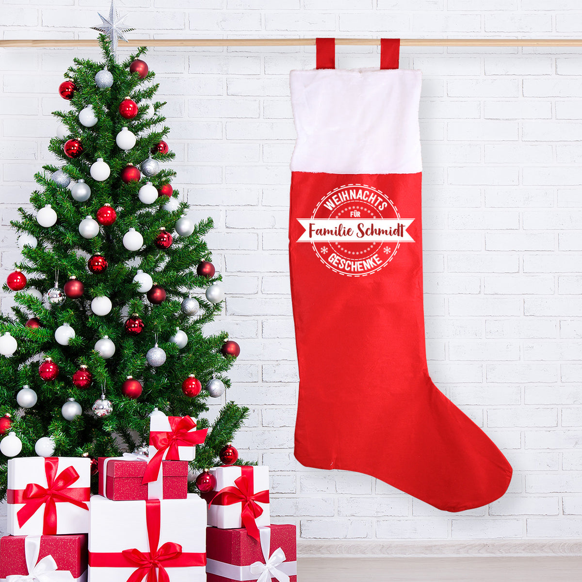 XXL Weihnachtssocke mit persönlichem Aufdruck "Familie Schmidt" hängend neben einem Weihnachtsbaum und Geschenken