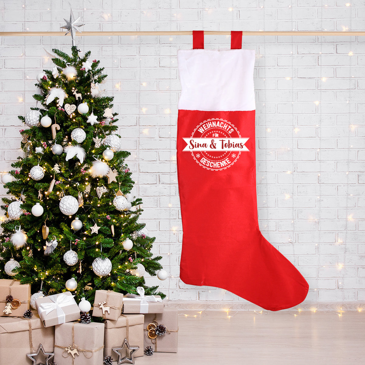 XXL Weihnachtssocke mit persönlichem Aufdruck "Sina & Tobias" hängend neben einem Weihnachtsbaum und Geschenken