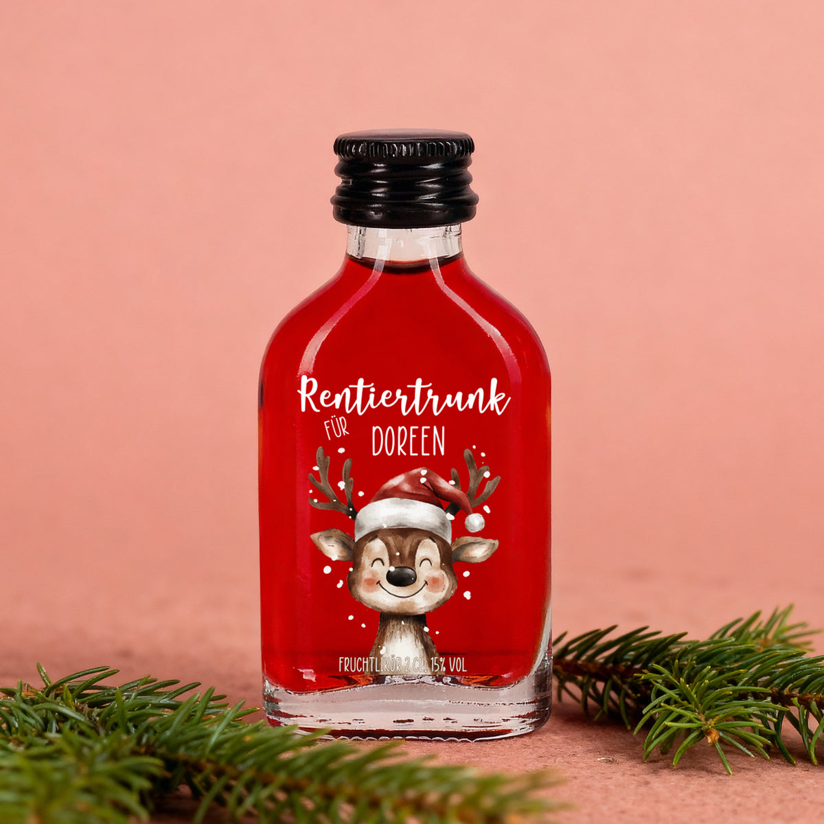 Fruchtlikör-Flasche „Rentiertrunk für Doreen“ auf rosafarbenem Hintergrund mit Tannengrün, winterliche Szene mit rotem Likör und liebevollem Etikett.