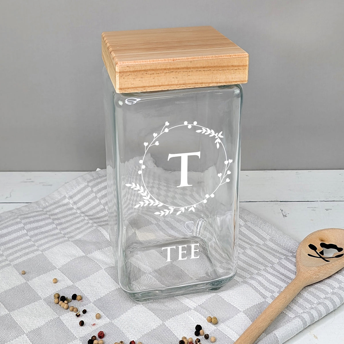 Teedose aus Glas mit weißem Motiv „T“ und Schriftzug „TEE“ auf Küchentuch