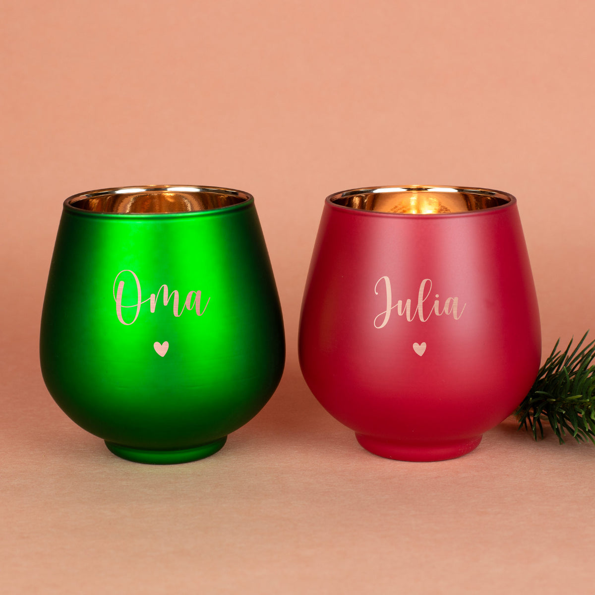 Zwei Windlichter in Grün und Rot mit Gravur „Oma“ und „Julia“ sowie kleinem Herzmotiv, festlich auf beigem Untergrund dekoriert.