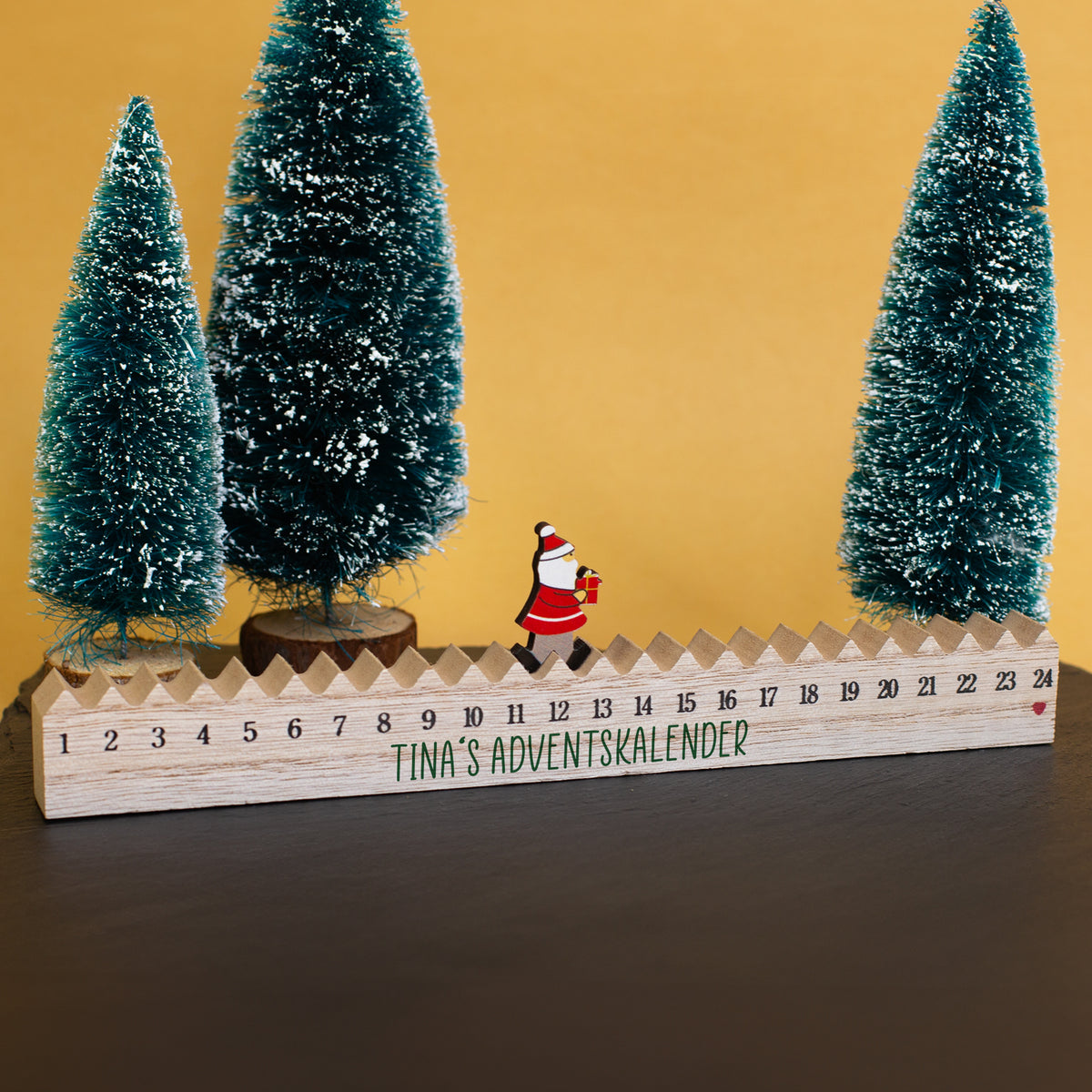 Adventskalender aus Holz mit Weihnachtsmann-Figur als Weihnachtsdeko zwischen Tannenbäumen