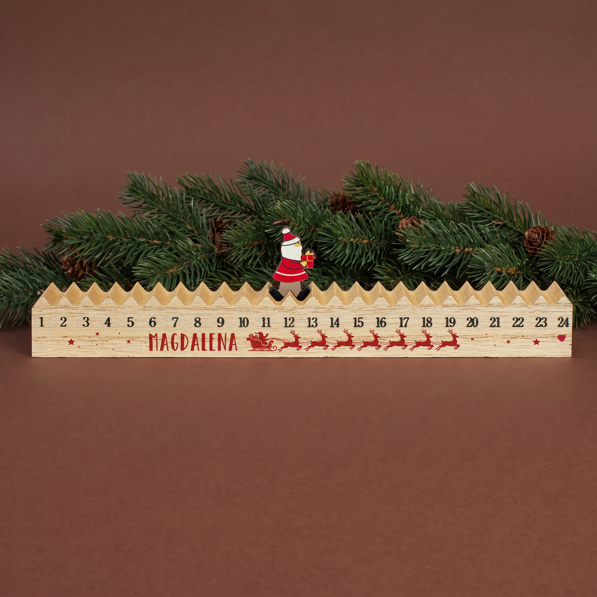 Personalisierter Walking-Santa-Weihnachtskalender „Magdalena“ aus Holz vor Tannenzweigen und weihnachtlicher Dekoration