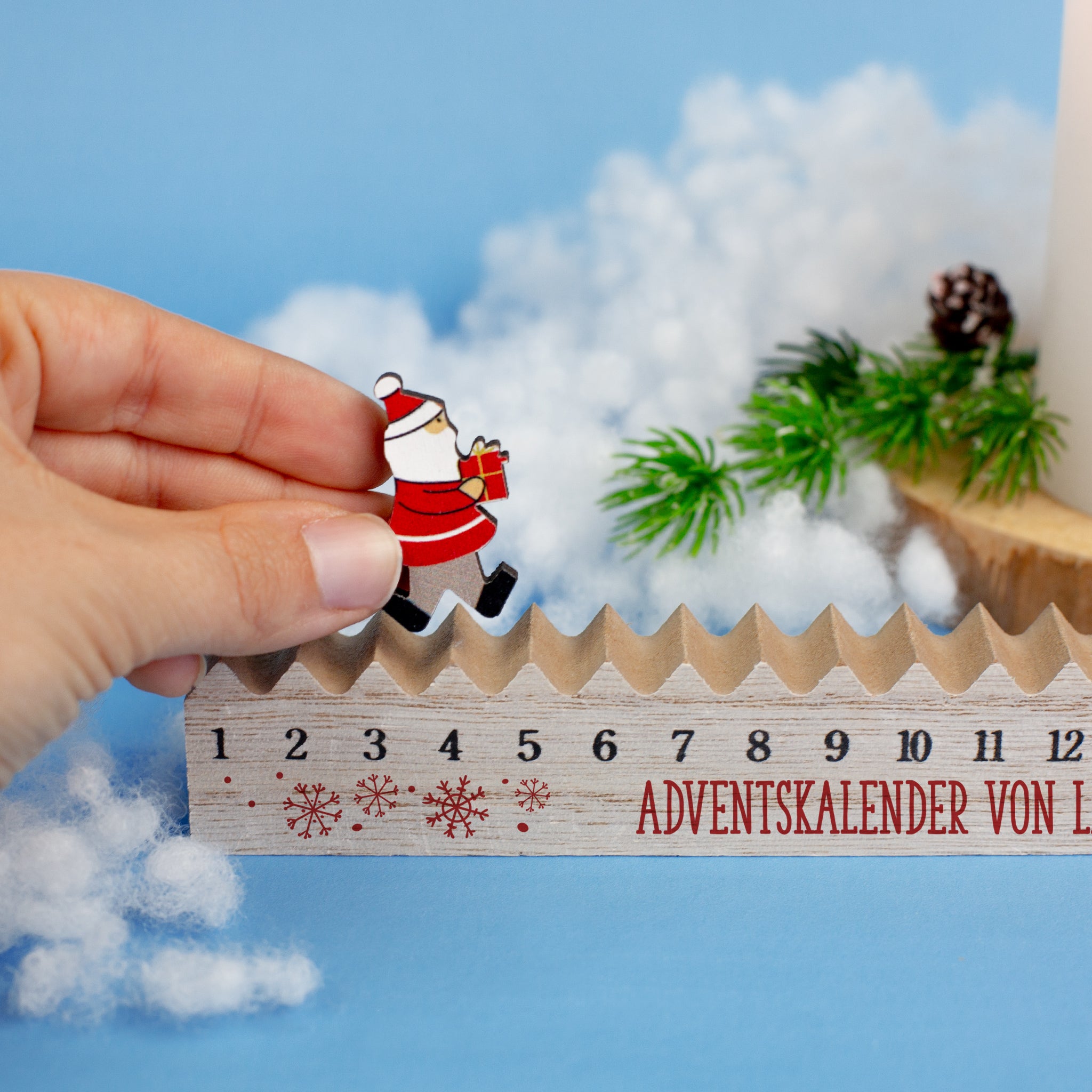 Hand bewegt Santa-Figur auf personalisierbarem Holz-Adventskalender mit roten Schneeflocken.