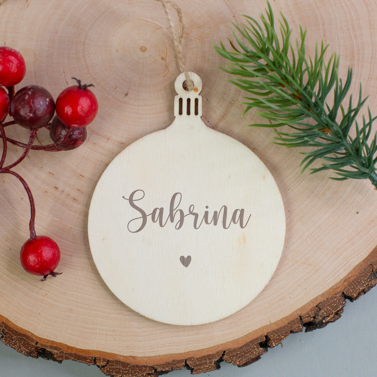 Personalisierter Holzanhänger in Kugelform mit Gravur „Sabrina“ und Herzsymbol, dekoriert mit Beeren und Zweig.