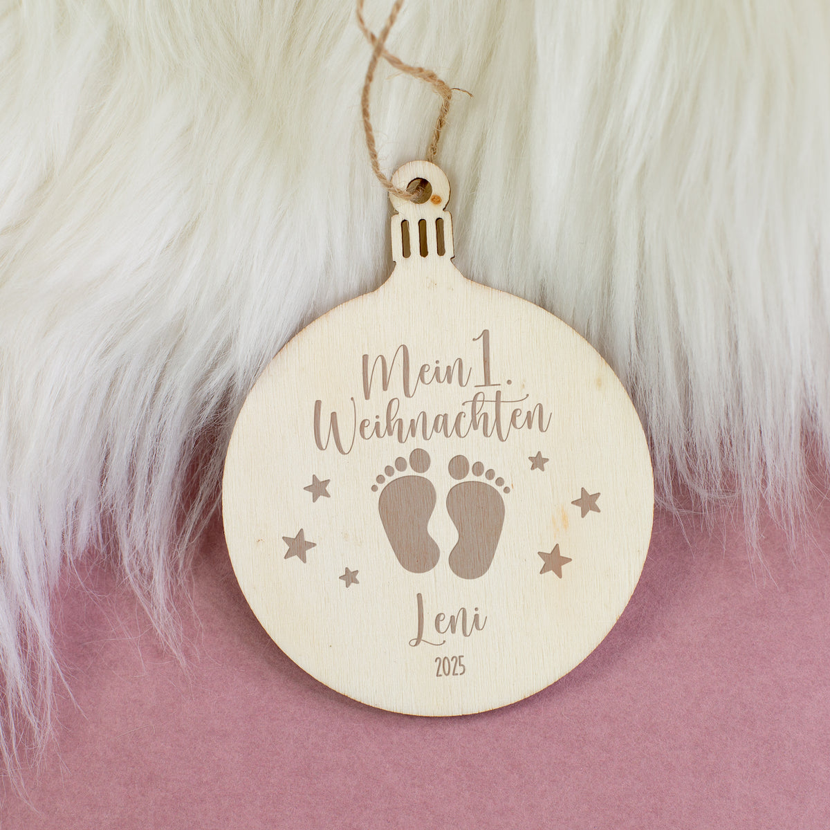 Holzanhänger „Mein 1. Weihnachten“ mit Namen und Jahr graviert, Motiv Babyfüße und Sterne, dekoriert auf weißem Fellhintergrund.