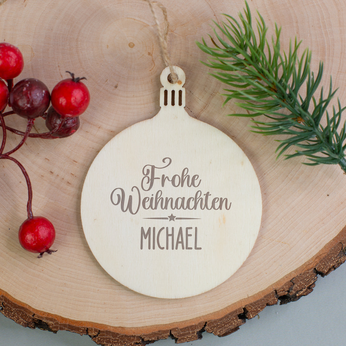 Holzanhänger in Tannenbaum-Form mit Gravur „Frohe Weihnachten Leonie“, dekoriert mit roten Beerenzweigen.