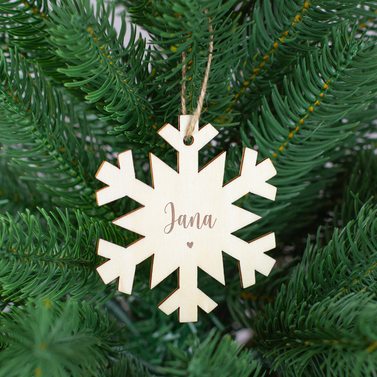 Schneeflocken-Holzanhänger mit Gravur „Jana“ und kleinem Herzmotiv, aufgehängt im Tannenbaum.