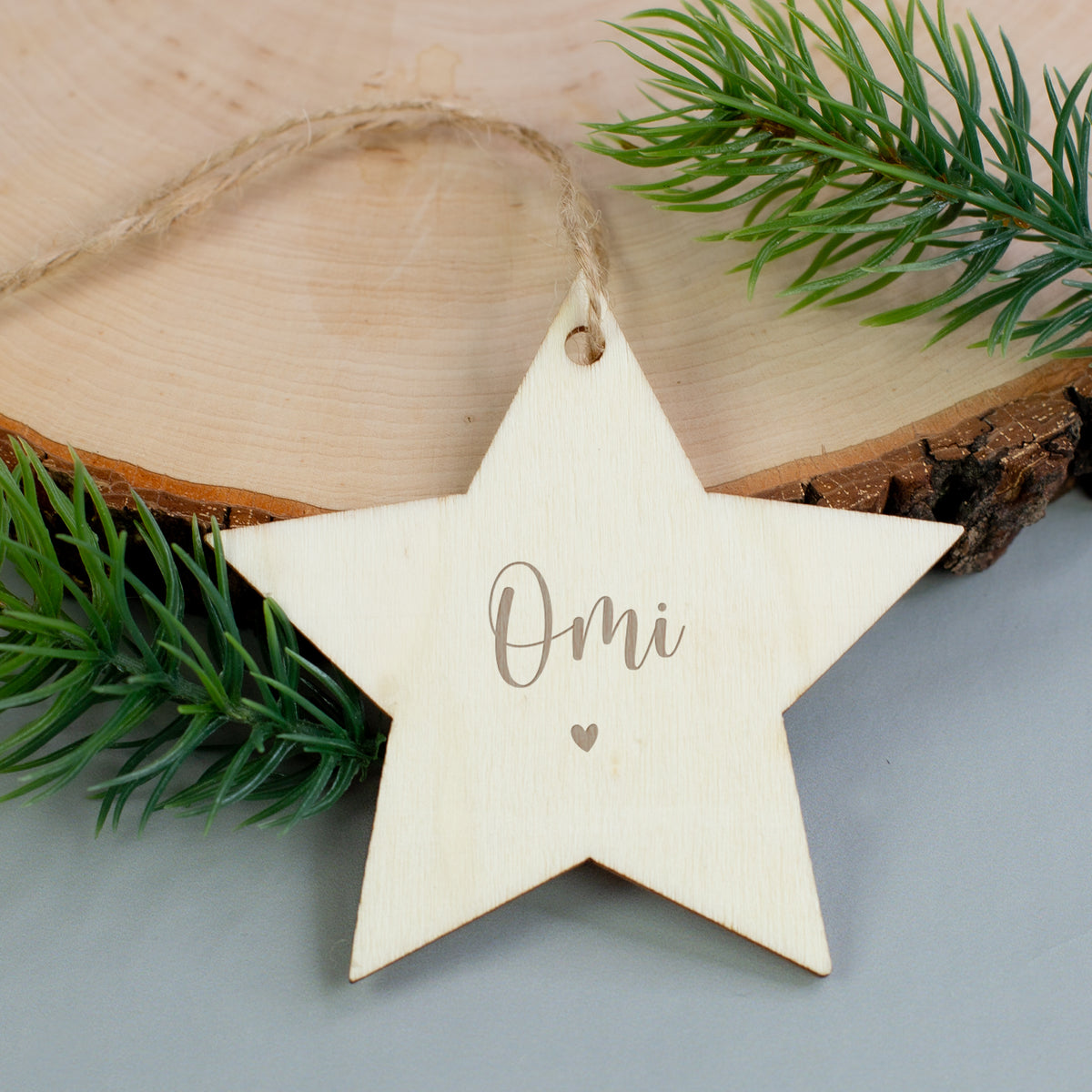 Holzstern mit Gravur „Omi“ und Herzmotiv, dekoriert mit Zweigen auf Holzuntergrund.